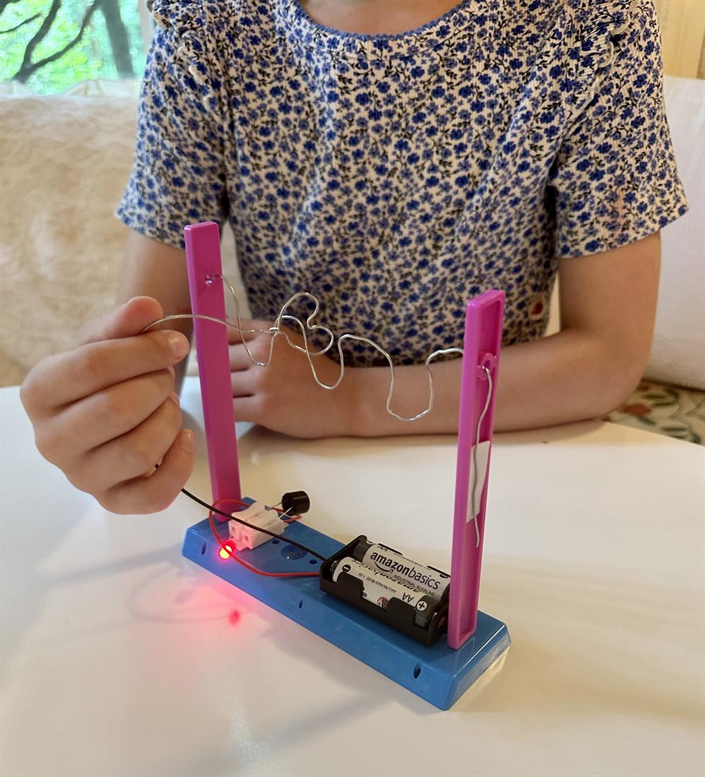 A child testing the buzz-wire game they built in an after-school engineering class